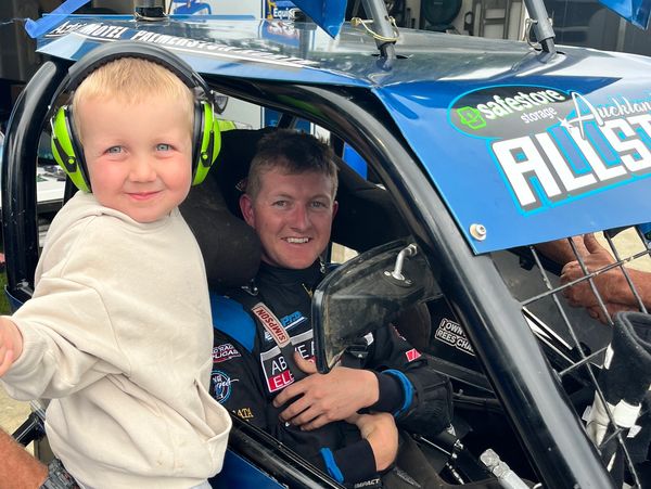 Young boy with headphones and a race car driver in a blue race car.