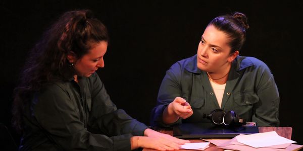 Two women in green shirts engaged in a serious discussion over documents.