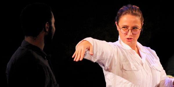 Woman in glasses gesturing expressively during a conversation with a man in dark clothing.
