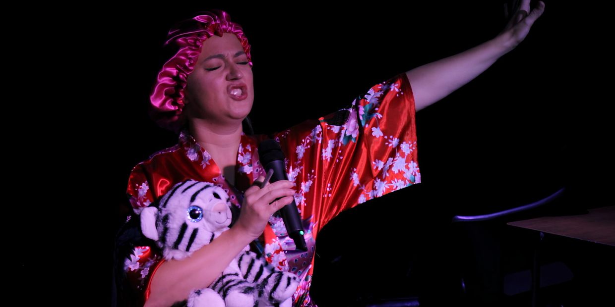 Person in a red floral robe and bonnet singing passionately while hugging a stuffed tiger.