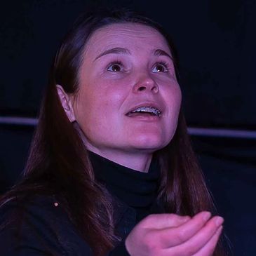 Woman with braces speaking or gesturing with hand under purple lighting.