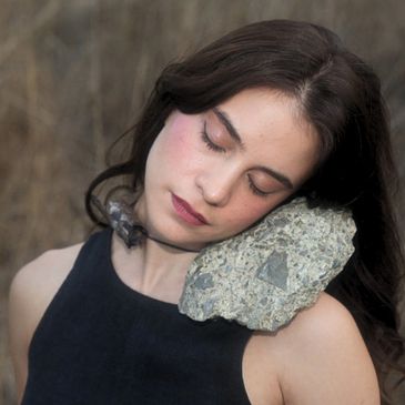 Woman resting her head on a large rock, eyes closed.