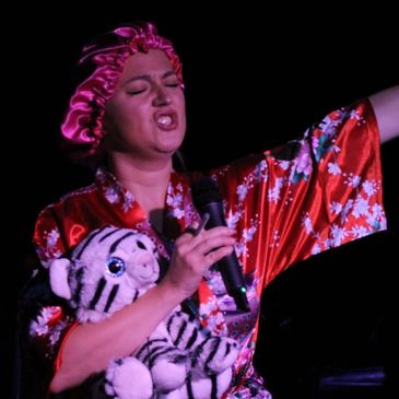 Person in a floral robe and satin bonnet passionately singing while holding a stuffed tiger.