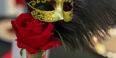 A golden masquerade mask with black feathers next to a red rose.