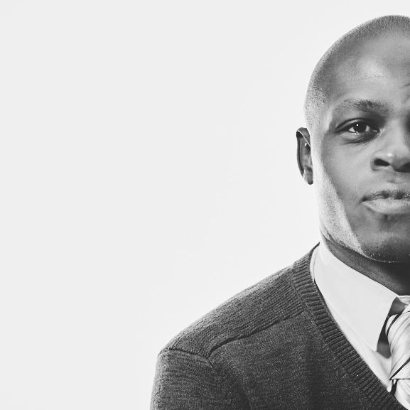 Black and white close-up of a serious man in a sweater and tie.