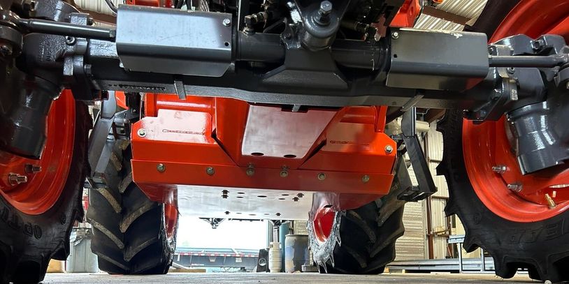 Close-up of the undercarriage of a red tractor with large tires in a workshop.