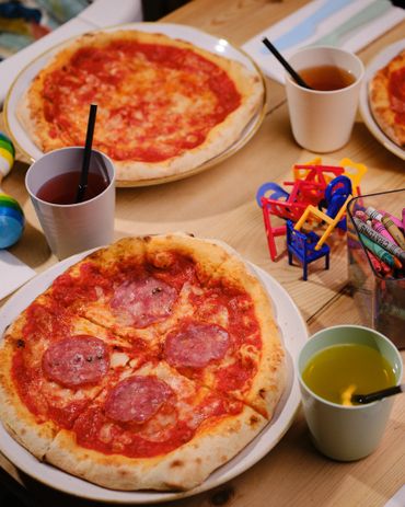 Mini pizzas with drinks and kids' crayons and toys on a wooden table.
