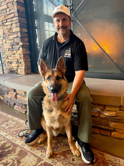 Man sitting by a fireplace with a German Shepherd dog.