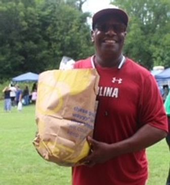 Man in red shirt holding a large paper bag outdoors.