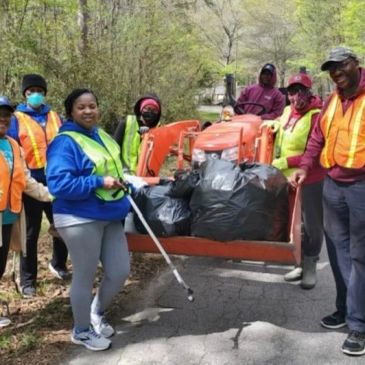 Group of volunteers with safety vests collecting trash outdoors.