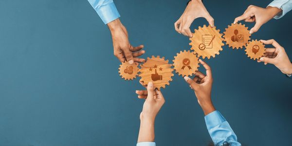 Hands connecting wooden gears with business and teamwork icons.