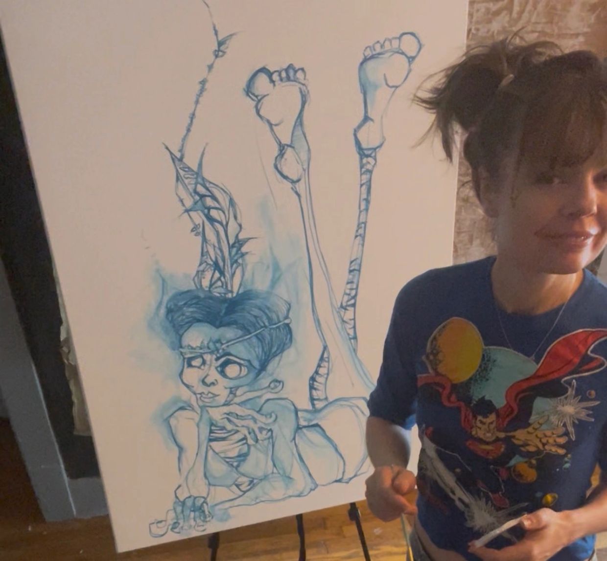 Woman posing next to a surreal blue sketch of a skeletal figure with exaggerated feet.