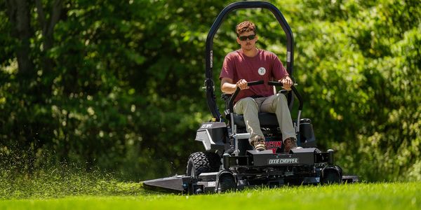 A man mowing a green lawn on a Dixie Chopper mower.