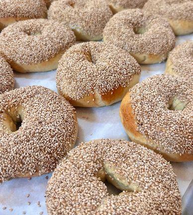 Freshly baked sesame-covered bagels arranged closely on a tray.