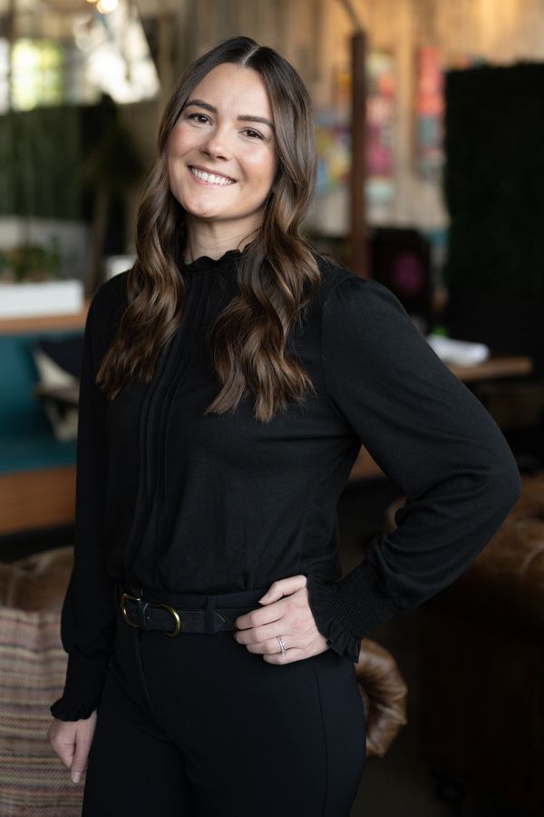 Young woman in black outfit smiling indoors with hand on hip.