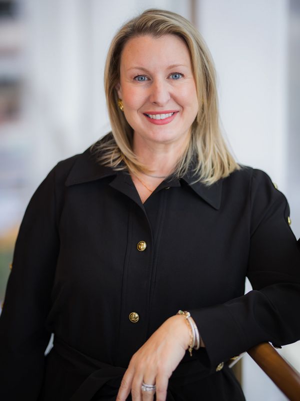 Smiling woman in a black coat posing indoors with a confident expression.