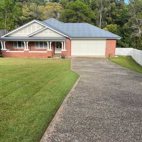 A brick house with a large driveway and green lawn.