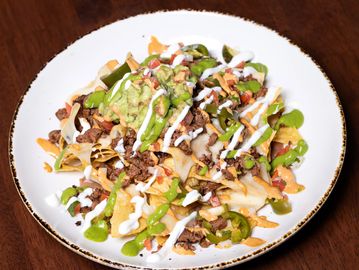 Plate of loaded nachos with meat, jalapenos, and sauces.