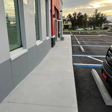 Empty sidewalk next to a building and parking lot during sunset.