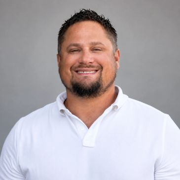 Man smiling in a white polo shirt against a gray background.