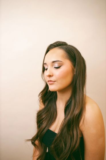 Young woman with long brown hair and closed eyes against a neutral background.