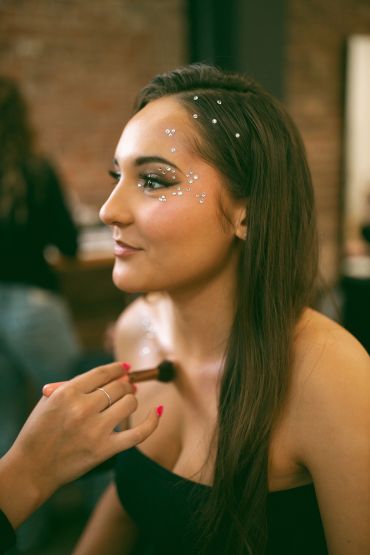 Woman with crystal face decorations getting makeup applied.