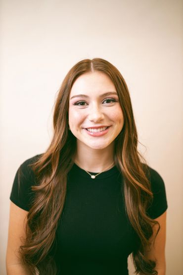 Young woman with long brown hair smiling at the camera.