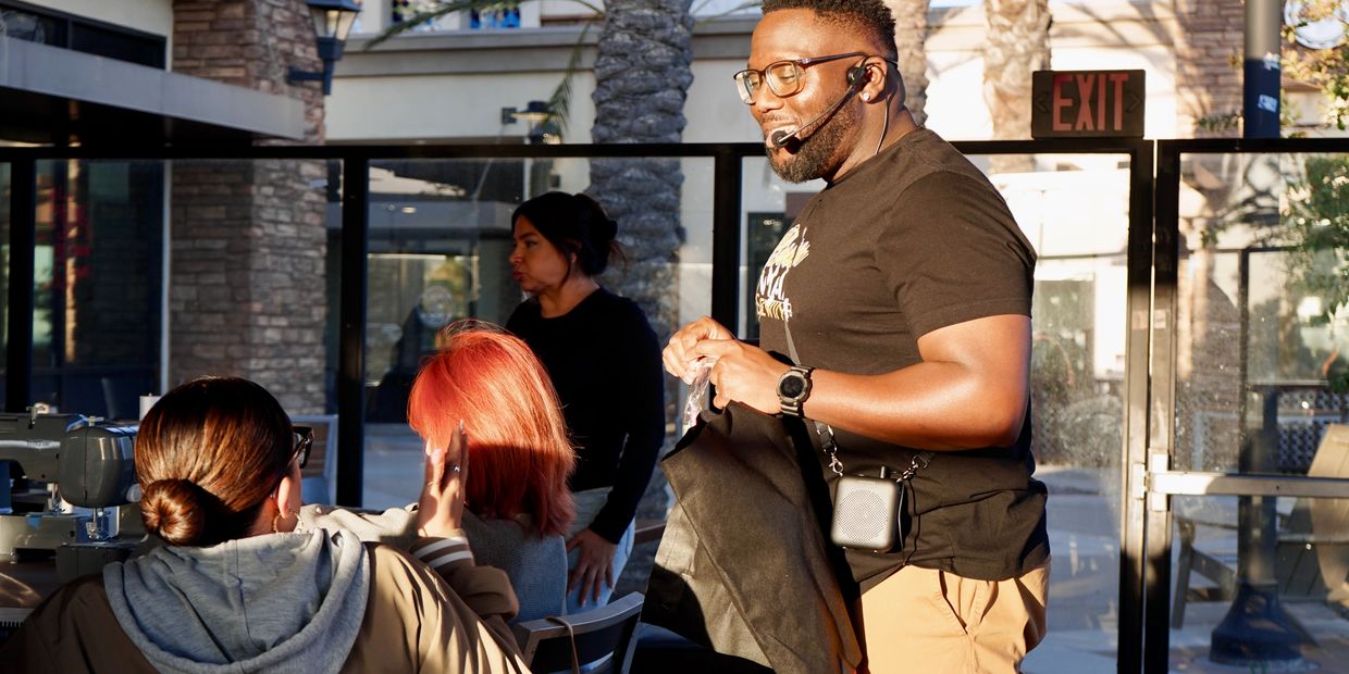 Man with headset speaking to seated women in a sunlit room.
