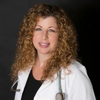 Smiling female doctor with curly hair wearing a white coat and stethoscope.