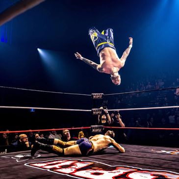 Wrestler performing a high-flying flip over opponent in the ring.