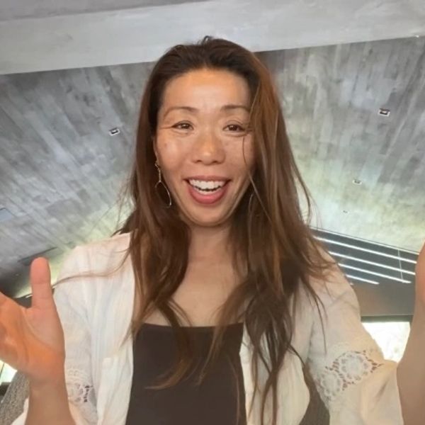 Smiling woman with long hair and a white cardigan indoors.