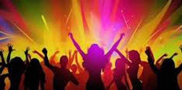Silhouetted crowd dancing energetically under vibrant colorful lights.