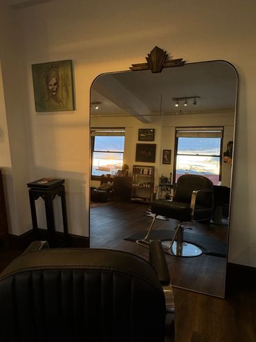 A stylish salon chair and large mirror reflecting a cozy interior space with windows.