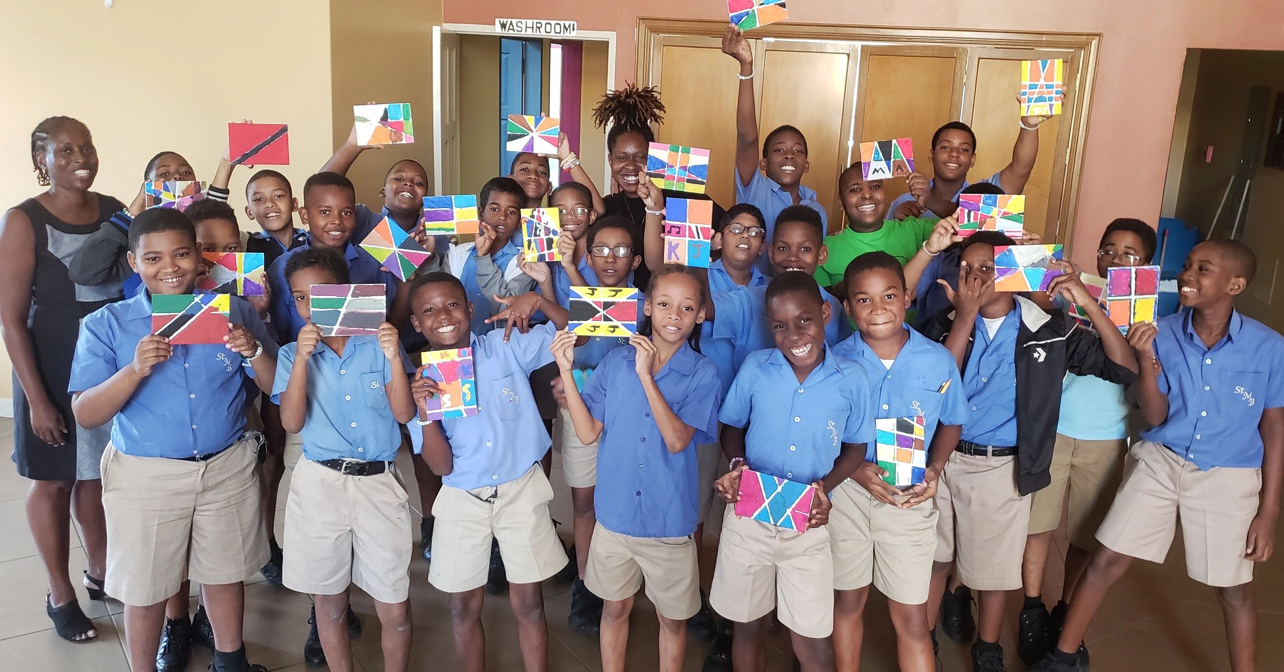 A group of school children proudly display colorful artwork in a classroom.