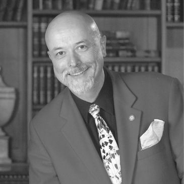 Magician Wayne Haarhaus smiles at the camera wearing a tie covered in playing cards.