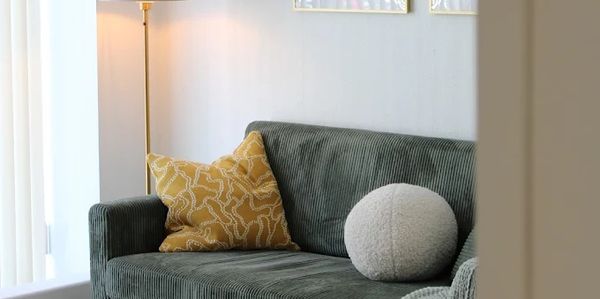 Cozy green sofa with yellow and round white cushions by a floor lamp.