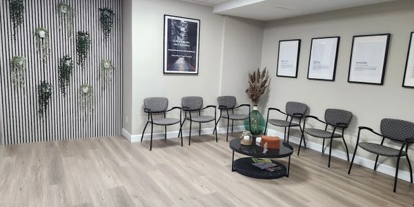Modern waiting room with chairs, a coffee table, and wall decor including plants and framed quotes.