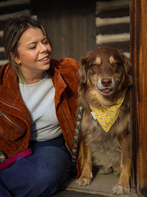 Woman smiling beside a dog wearing a yellow bandana.