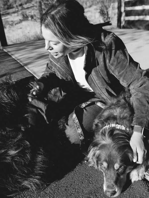 Woman playing with two dogs outside on a paved surface.