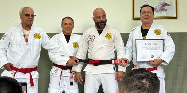 Four men in martial arts uniforms with black and red belts, one holding a certificate.