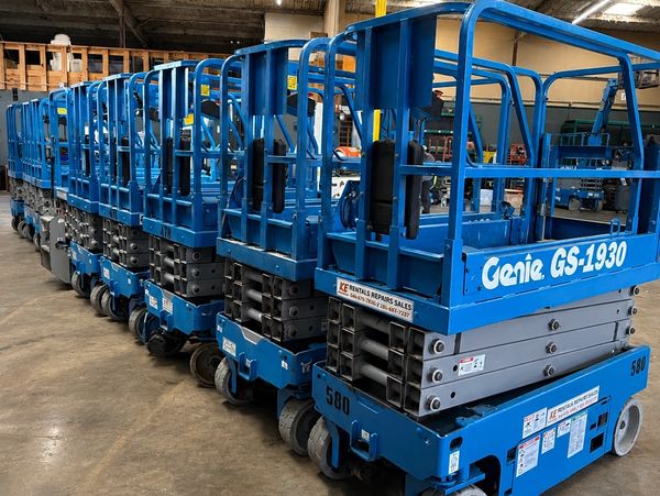 A row of blue Genie GS-1930 scissor lifts in a warehouse.