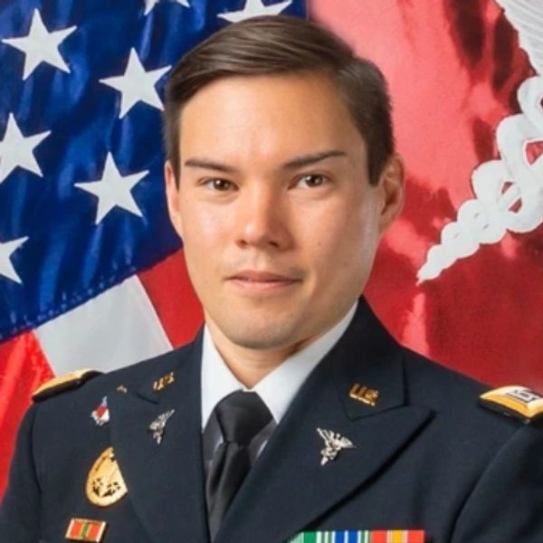 Military officer posing with American flag backdrop.