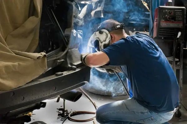 A welder working on a vehicle with protective gear in a workshop.