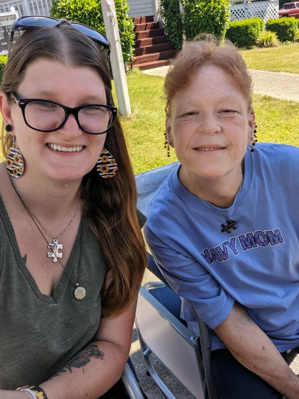 Two women smiling outdoors, one wearing a "NAVY MOM" shirt.