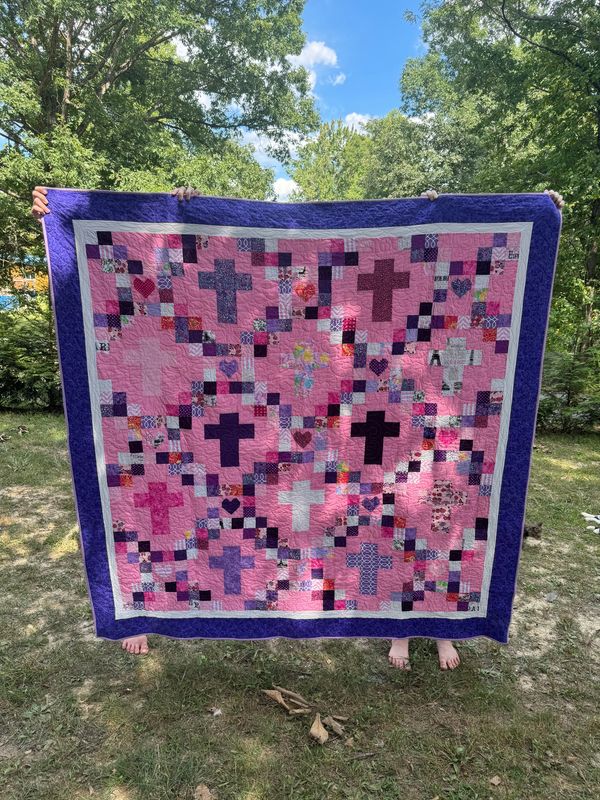 A mostly pink and purple quilt with crosses and hearts. 