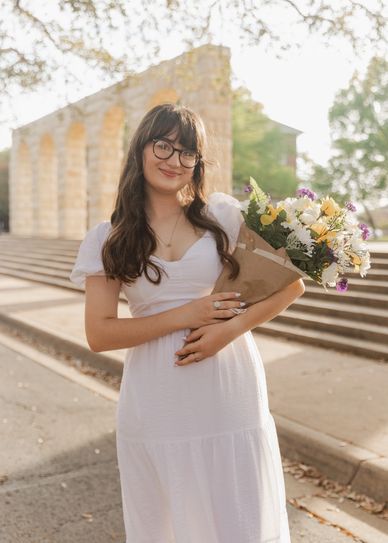 Young woman in white dress holding bouquet of flowers.