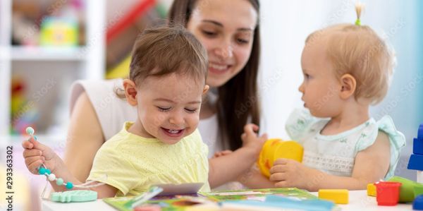 Picture of young female teacher with long dark hair playing with two happy toddlers 