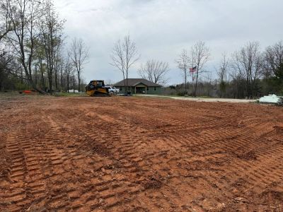 Freshly leveled dirt land with a bulldozer near a small building and flagpole.