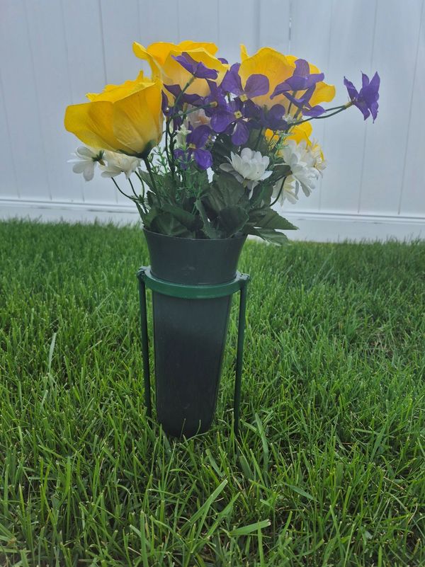 A black vase with yellow, purple, and white flowers in green grass.
