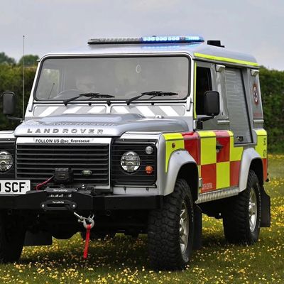 Land Rover fire rescue vehicle with blue lights on grassy field.